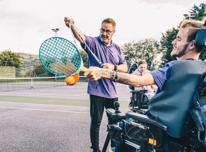 A care worker playing tennis with a care user in a wheelchair