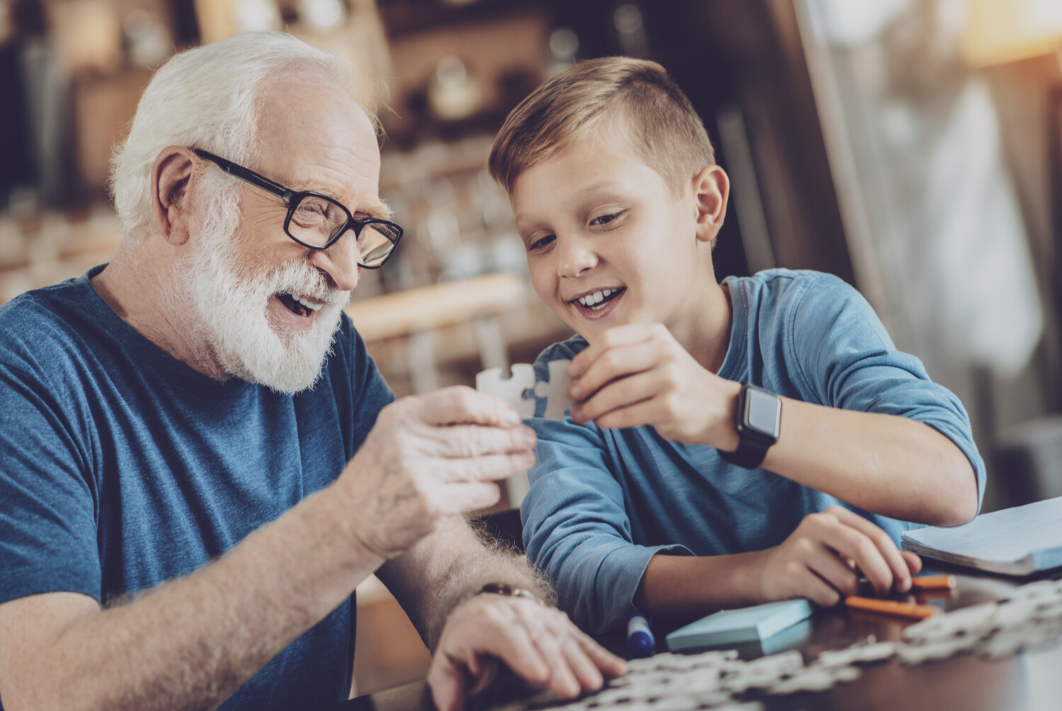 Older man doing a jig saw with a young boy, both are smiling