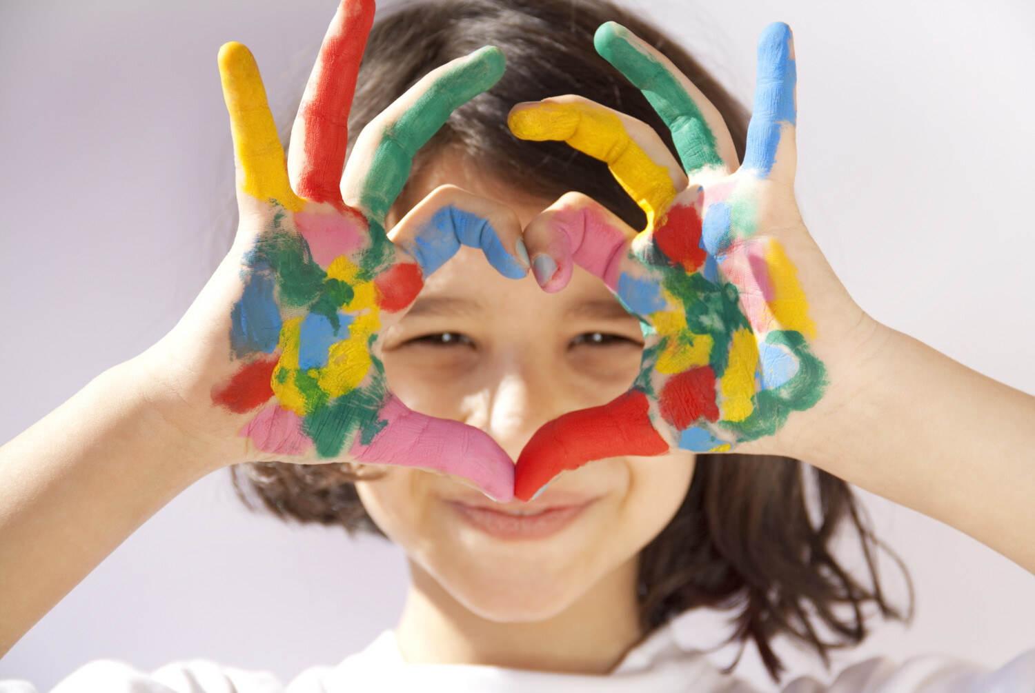 Girl with paint on her hands making a heart shape with her hands