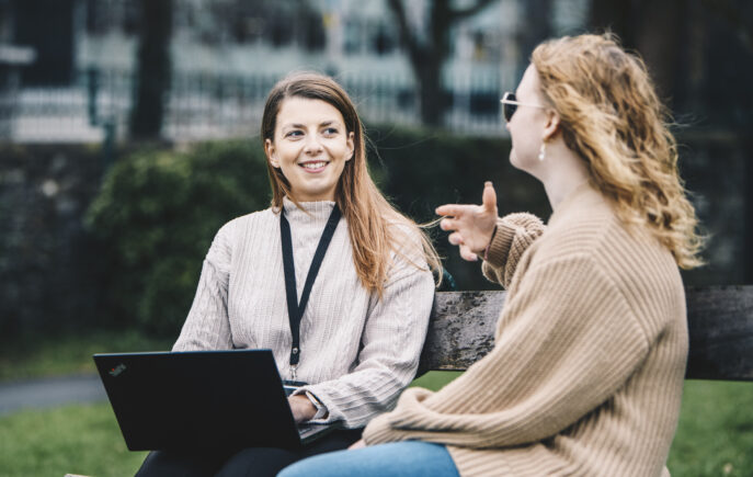 Ruby sat on a bench outside with her laptop smiling in conversation with her care user