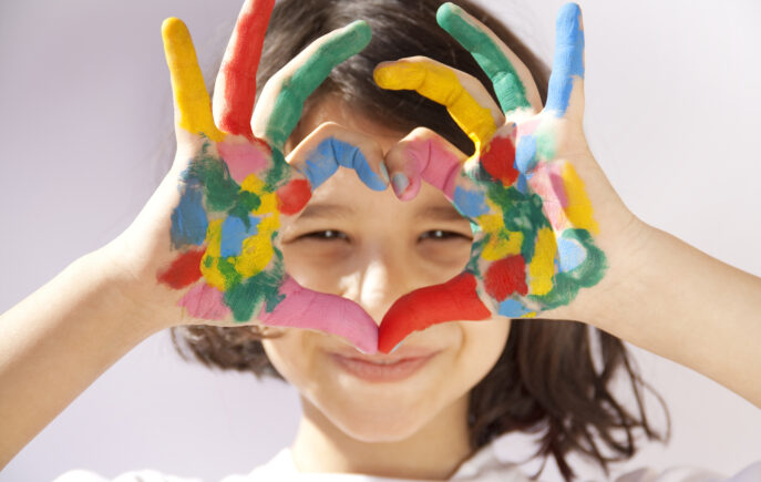 Girl with paint on her hands making a heart shape with her hands